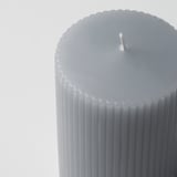 Close-up of elegant gray pillar candle with vertical grooves, unlit wick, smooth texture.