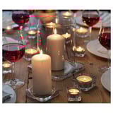 A dinner table with white candles in clear glass holders and wine glasses with red wine.