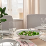 Table set with white plates, glasses, and a bowl of salad, ready for dining.
