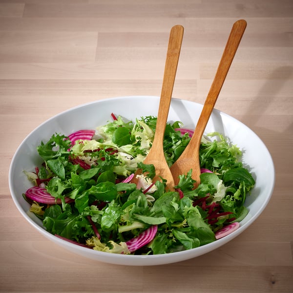 A large bowl of fresh green salad with wooden tongs on a wooden table.