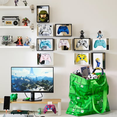 Green GÖTEHULT bag with gaming gear, controllers, figures, and gold helmet above monitor.