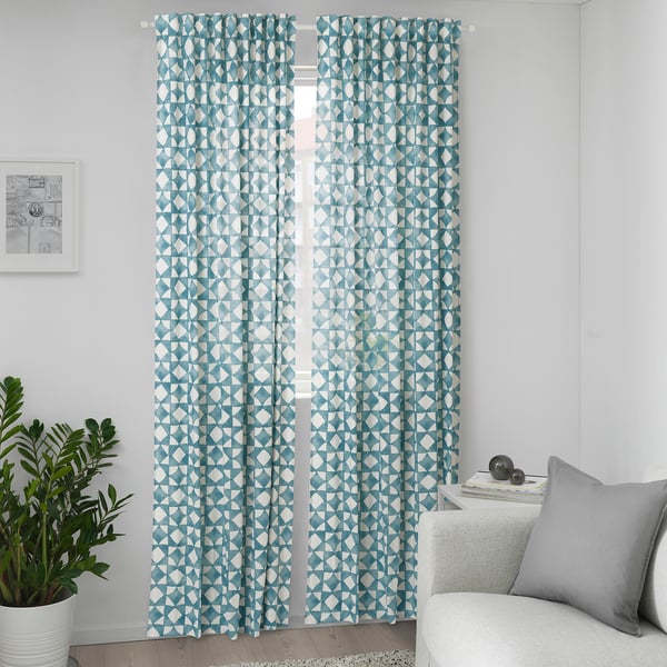 Blue geometric curtains hang by window, taller than couch, beside plant, adding playful pattern.