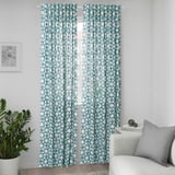 Blue geometric curtains hang by window, taller than couch, beside plant, adding playful pattern.