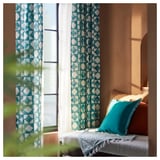 Cozy bedroom with green patterned curtains and teal pillow, letting in soft light.