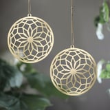 Two golden ornate sphere ornaments hang on green foliage, GOKVÄLLÅ collection.