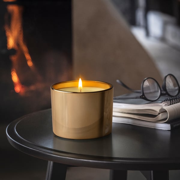 Lit candle in glass on table, beside glasses and notebooks, creating warm atmosphere.