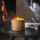 Lit candle in glass on table, beside glasses and notebooks, creating warm atmosphere.