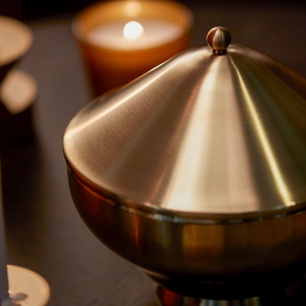 Elegant metallic bowl with conical lid, reflecting warm light. Ideal for serving and displaying food.