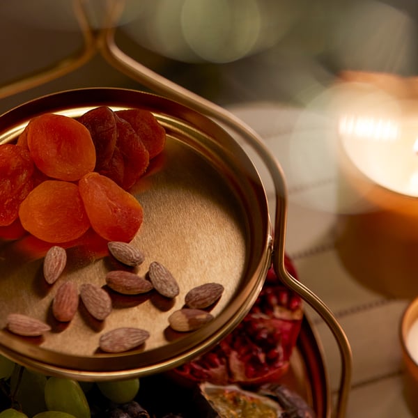 Metal serving tray with dried apricots and almonds, lit candle nearby.