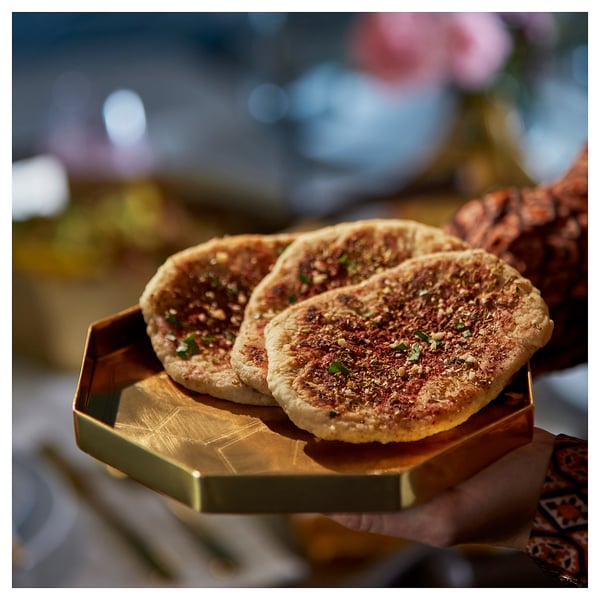 Octagonal gold-colored serving tray holding flatbreads with herbs, stylishly presented.