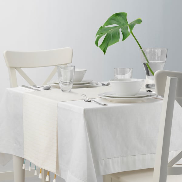 White table set with dishes and runner with tassels.