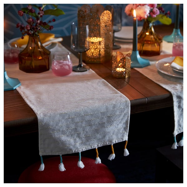 Table set with beige GOKVÄLLÅ runner, tassels, glasses, candles, flowers, and plates.