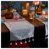 Table set with beige GOKVÄLLÅ runner, tassels, glasses, candles, flowers, and plates.