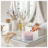 Light purple GOLIATTUJA scented candle being lit by hand. Glass holder, cotton wick, lavender scent. Surrounded by vanilla decor.