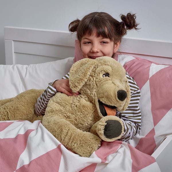 Young girl lying in bed, hugging large beige plush dog stuffed animal.