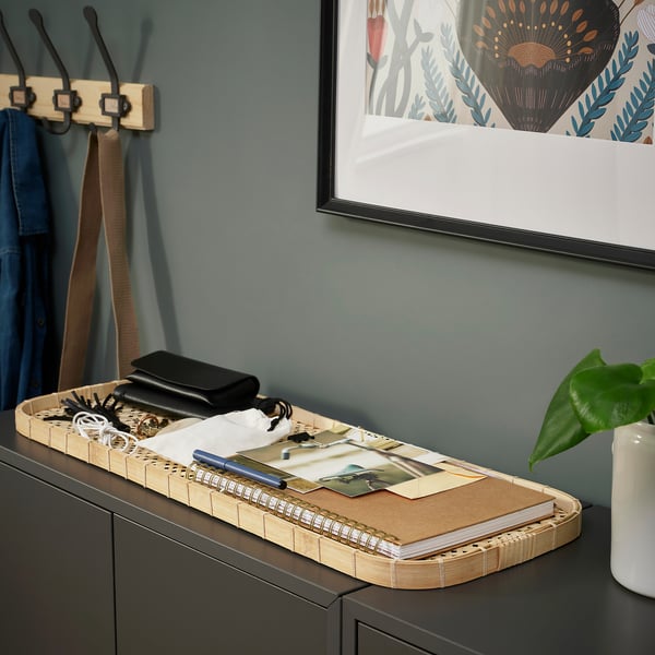 Tray organizes items on dark cabinet, includes wallet, keys, and notebook against green wall.