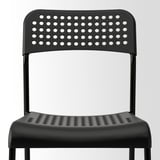 Black plastic chair with perforated seat and backrest, likely part of a stackable set.