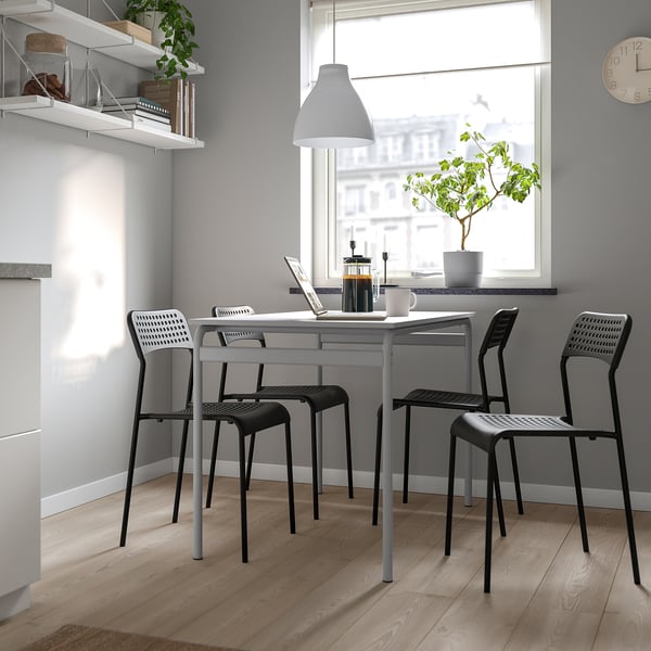 Modern dining set with grey table and black chairs, positioned near a window; chairs are stackable, complementing minimalist decor.