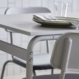 Modern grey metal table with minimalist design, holding a green plate and folded napkin. Perfect for compact dining spaces.