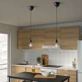 Small black pendant lights hang from the ceiling, illuminating a kitchen island with wooden cabinets and white tiles.