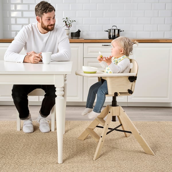 Man sits at table with coffee, child in highchair eats opposite.