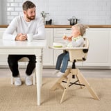 Man sits at table with coffee, child in highchair eats opposite.