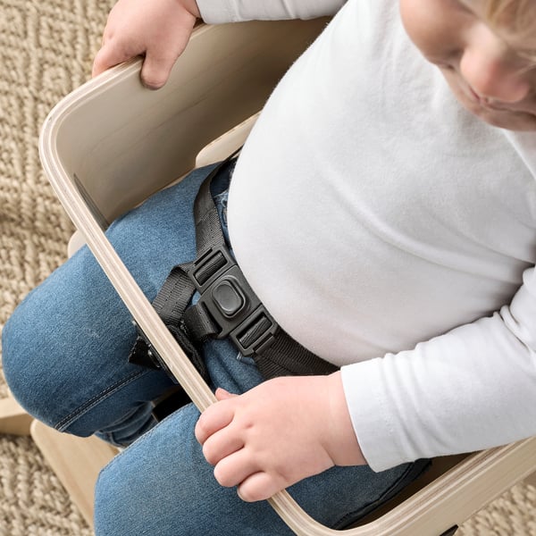 Child in highchair, secured by safety belt. Belt designed to avoid pinching.