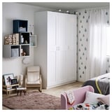 Modern bedroom with white GRIMO wardrobe, pink bed, colorful pillows, wooden chair, rug, and wall shelves.