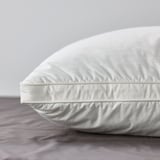 Close-up of a plush, white pillow on grey sheets, showcasing soft cotton and comfy design.