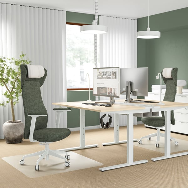 Modern office with 2 green GRÖNFJÄLL chairs, adjustable desks, monitors, large window, curtains, plant, side table.
