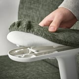 A hand lifts a white, adjustable lumbar support pillow from a green office chair, showing its ergonomic support feature.