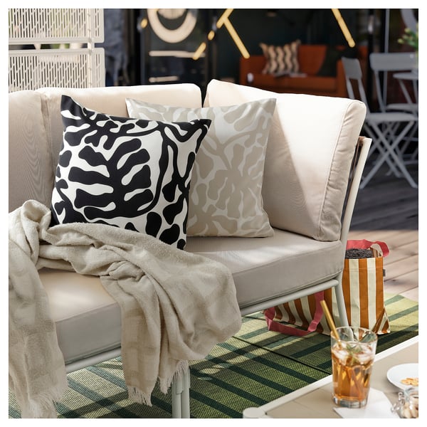 Outdoor sofa with GRÖNKNAVEL throw & patterned cushions. Eco-friendly, with a striped table and drink.