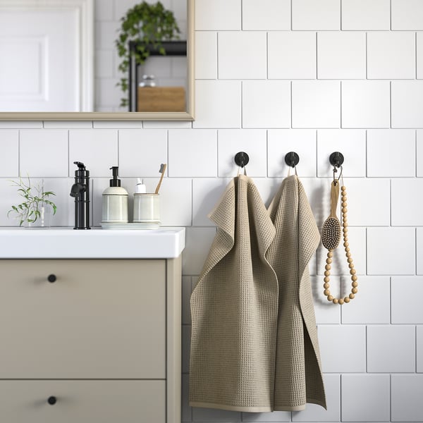 Modern bathroom with beige towels, white sink, black dispensers & plant.