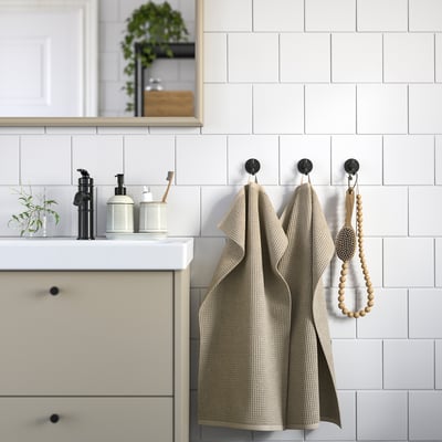 Modern bathroom with beige towels, white sink, black dispensers & plant.