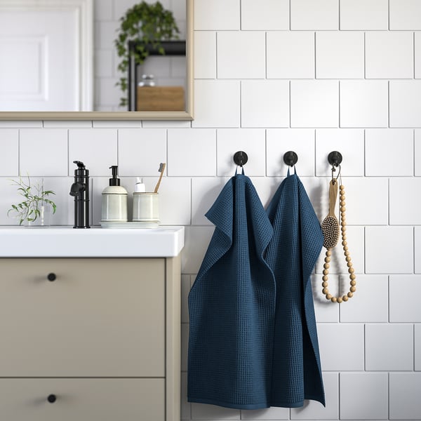 Modern bathroom with navy GULLDYNA towels on matte black hooks, beside cream cabinets and white tiles.
