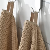 Beige towels hang neatly; soft, absorbent, cotton; ideal for everyday use.