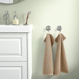 Beige GULVIAL towels hang on hooks near white cabinet and sink. 100% cotton, soft, medium-thick.