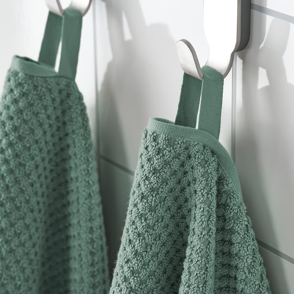 Two green, textured towels hang neatly on white hooks, showcasing their soft, absorbent material designed for frequent use.