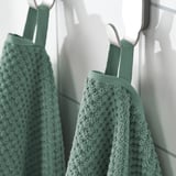 Two green, textured towels hang neatly on white hooks, showcasing their soft, absorbent material designed for frequent use.