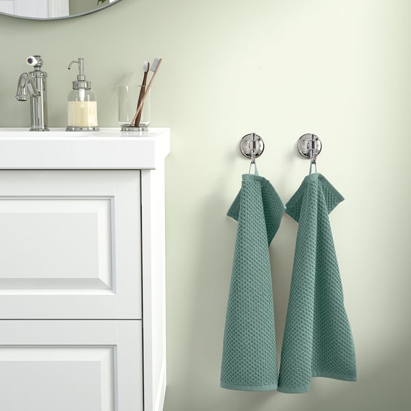 Teal towels hang on chrome hooks by white vanity on green wall.