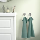 Teal towels hang on chrome hooks by white vanity on green wall.