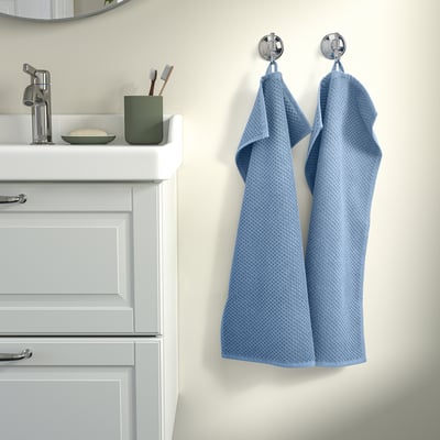 Blue towels hang on hooks beside white vanity with mirror.