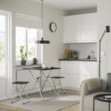 Modern kitchen with GUNDE table, white cabinets, gray counters, black accents, large window, cozy chair & throw.