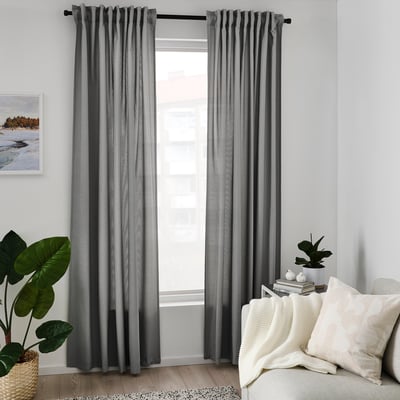 Grey curtains hang beside white couch with pillows, blanket, plants. Tall, draped, recycled polyester.