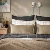 Bed with GURLI black & beige grid pillows and neutral bedding; pillows larger than small vase.