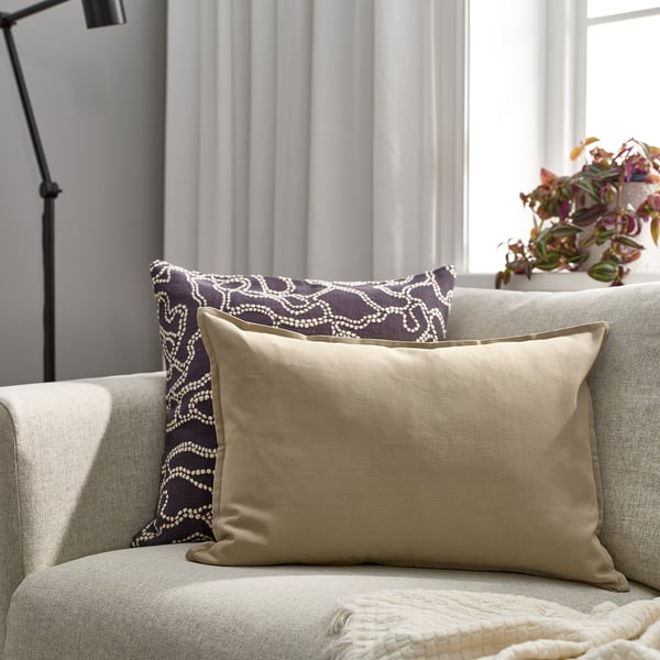 Beige GURLI throw pillow on cushioned chair, medium size, next to dark patterned pillow.