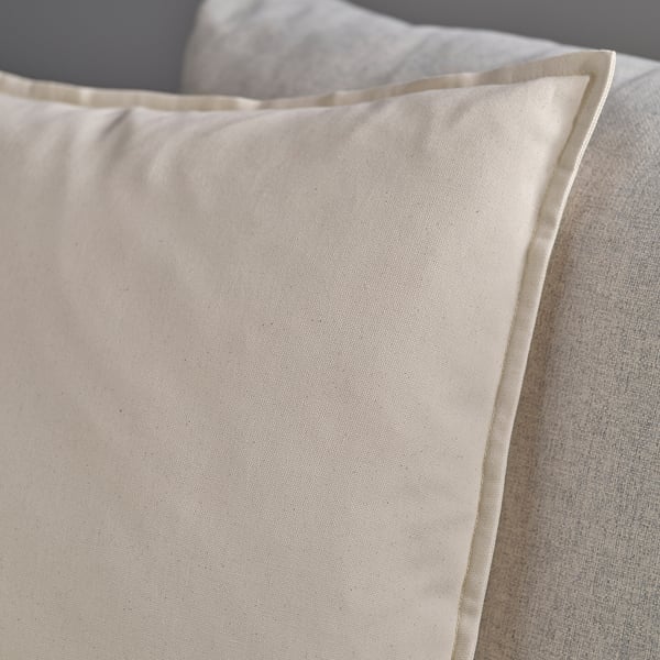 Cross-stitched pillow cover, light ivory, soft to touch, zipper closure, resting on a textured surface.