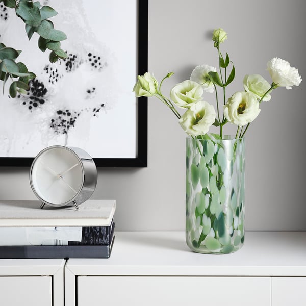 Green glass vase with white carnations, books & clock.