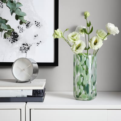 Green glass vase with white carnations, books & clock.