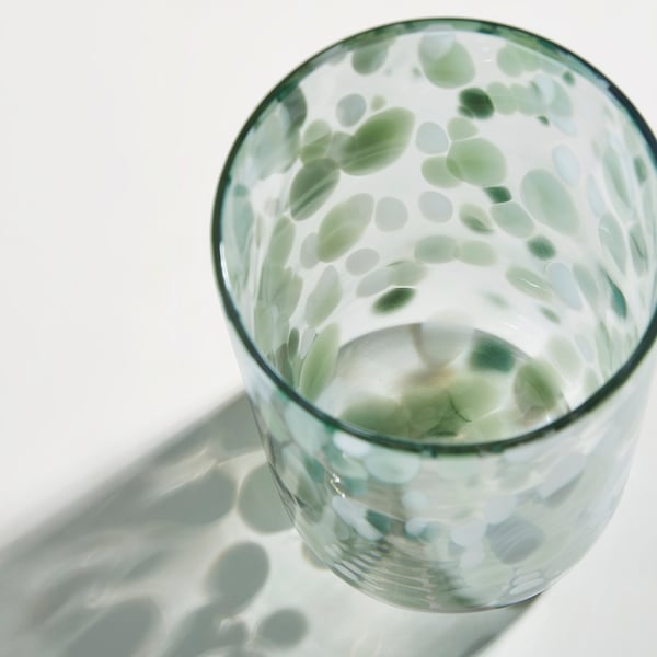 Glass vase with green and white dots, reflecting light. Well-made, with a smooth, clear texture.